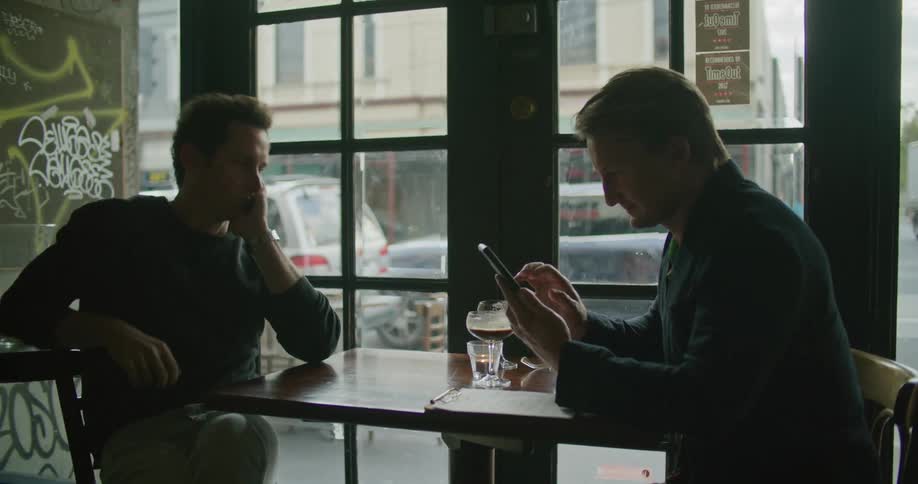 Two male friends looking at a smartphone on the table of a dimly lit restaurant