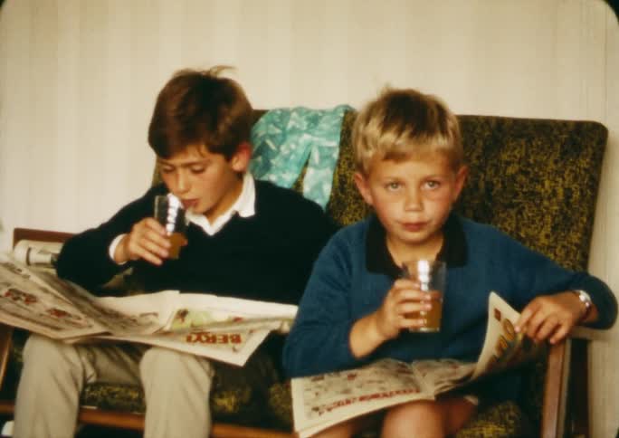Two young boys sit and read the comics while drinking a beverage
