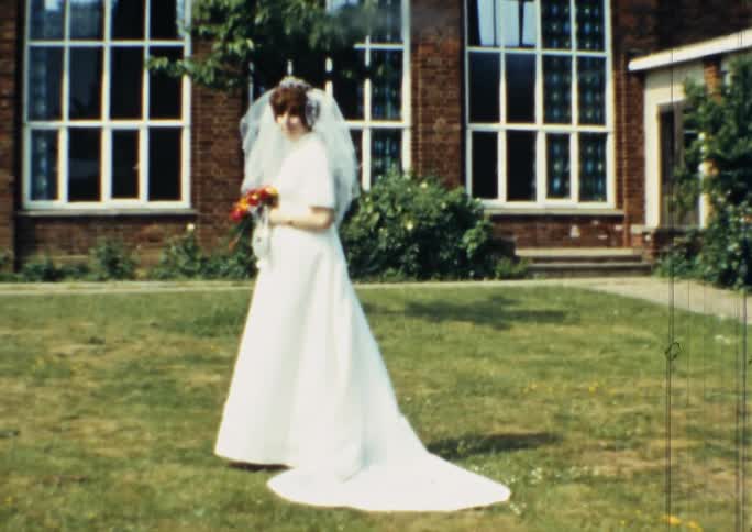A bride wearing a wedding gown poses with her flower bouquet outside on grass