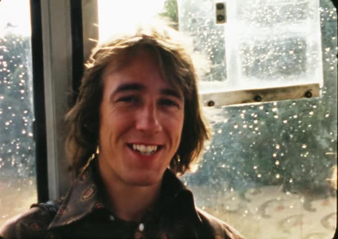 Man laughing and talking to someone while sitting close to a window