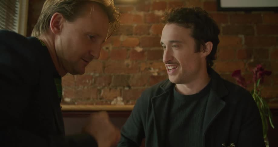 Two men chat while looking at a smartphone together in a restaurant