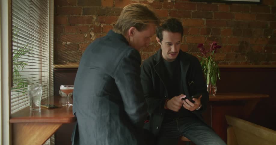 Two men in a bar talk and look at a cell phone