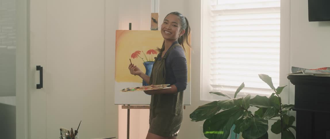 Woman painting on an easel indoors while smiling