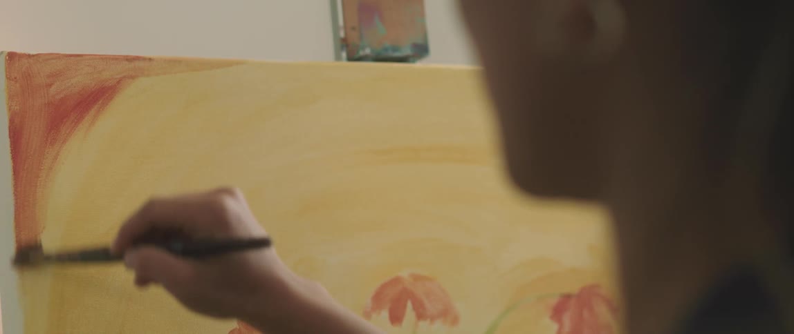 A woman stands at an easel painting with a paintbrush