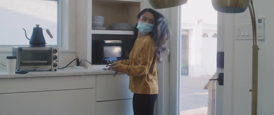 A woman walks into a kitchen picks up her keys and phone then leaves through a glass door