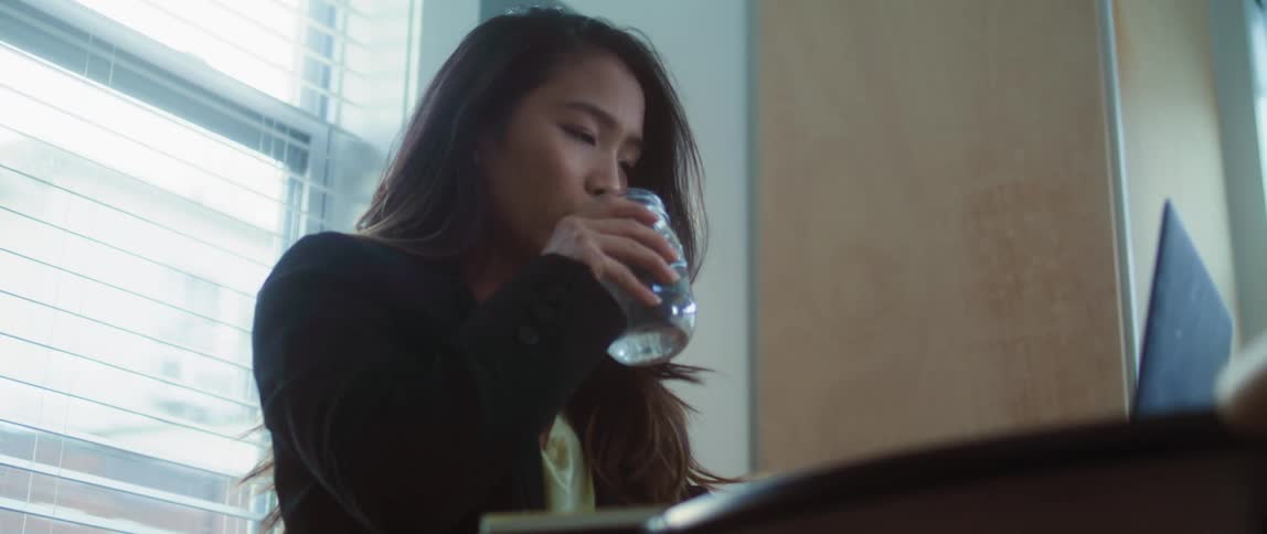 A woman drinking water from a mason jar while working at the office