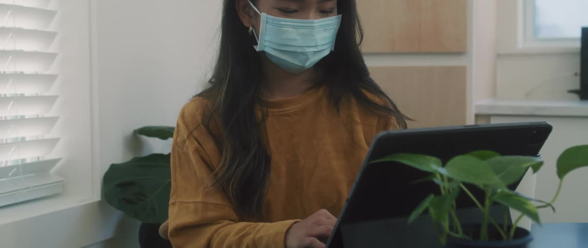 A woman sways as she sits and works on her laptop while wearing a mask