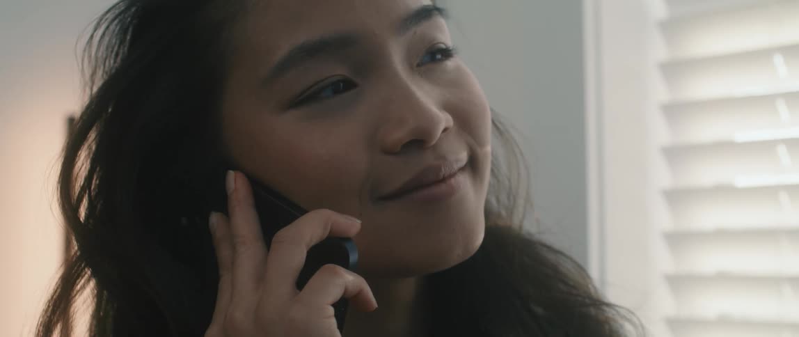 Young long haired girl smiles and laughs talking on her smartphone in a room at home