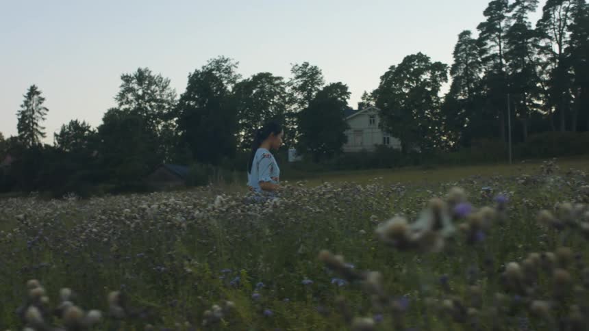A young asian woman walks through a meadow in a rural area in the evening