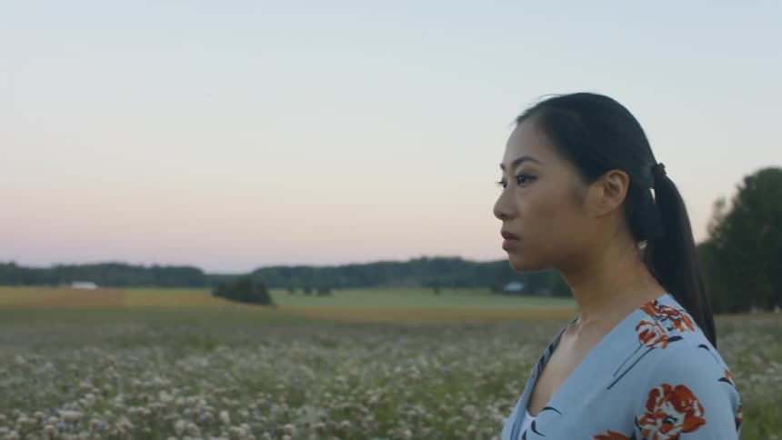 A woman walks through a field while looking around