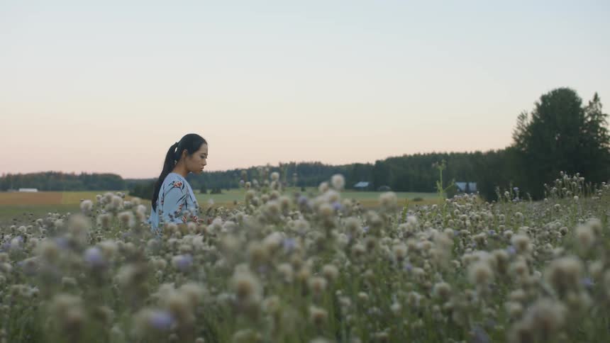 A young woman walking through a field of flowers in a rural area