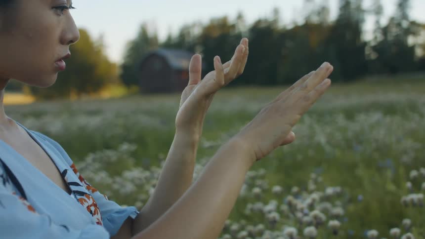 A woman examines her hands while standing in a field