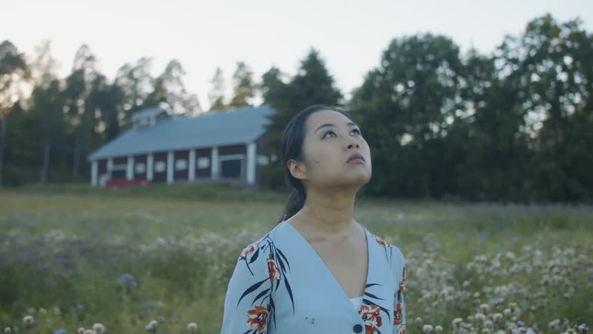 A young woman standing in a field of flowers in a rural area looking around
