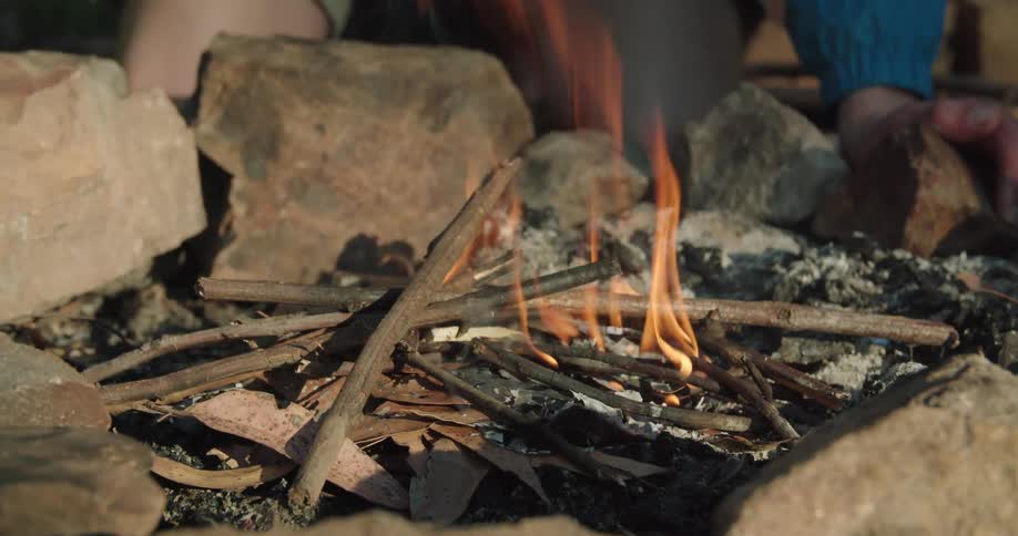 A man stoking the fire on a campfire with sticks
