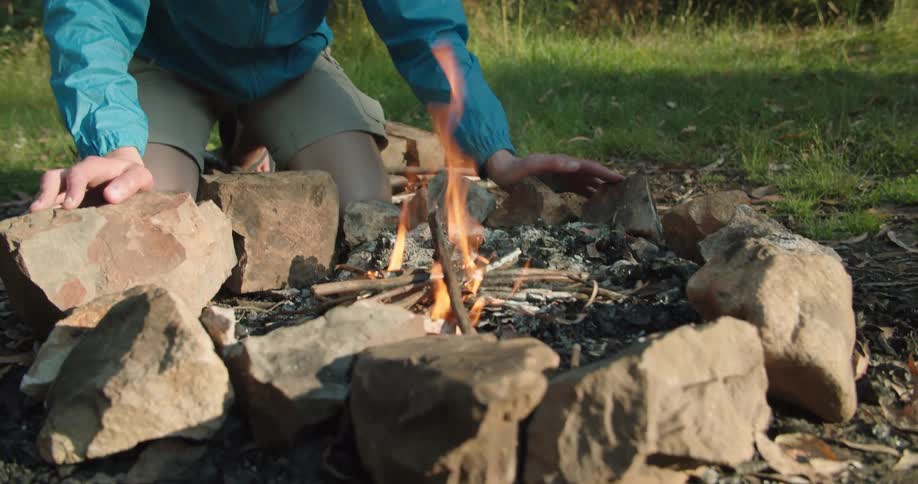 Man stoking a fire on an outdoor fire pit near the woods at day time