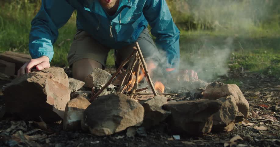 A man blows on a fire a small fire as the starts it