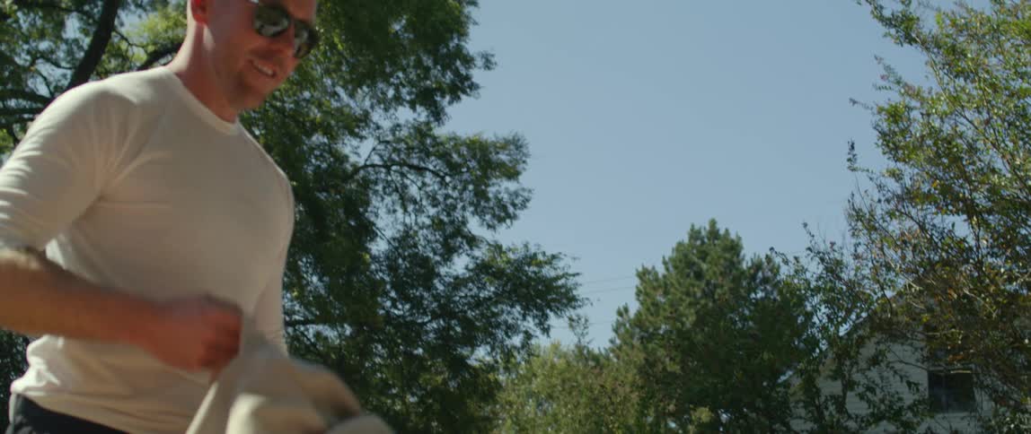 A man with sunglasses and a woman opening up a sheet with trees the sky and clouds in the background