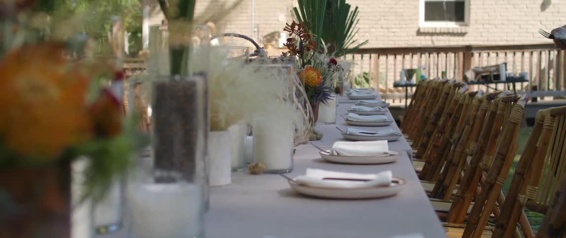 A person setting up a long dining table with flowers and candles and plates and utensils