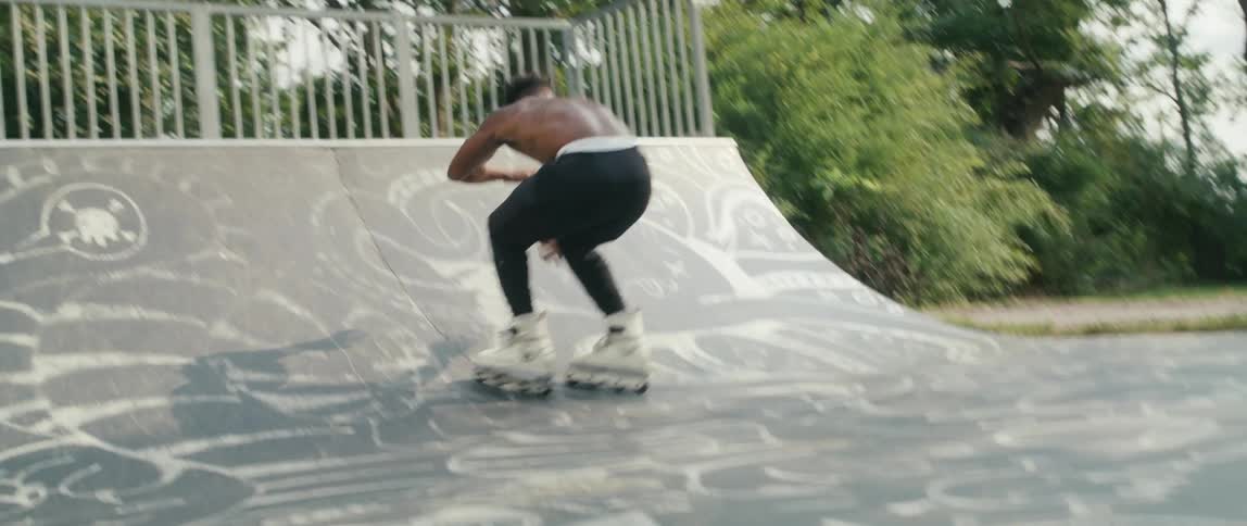 Shirtless sweaty strong muscular young man jumping ramps on inline skates in a park