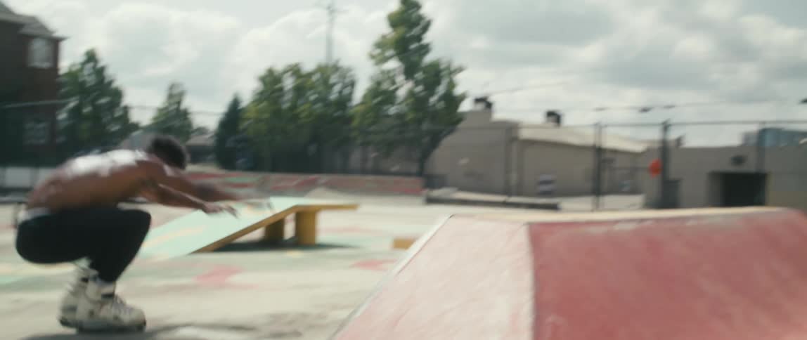 A shirtless man jumps and twirls off a ramp in an empty skate park