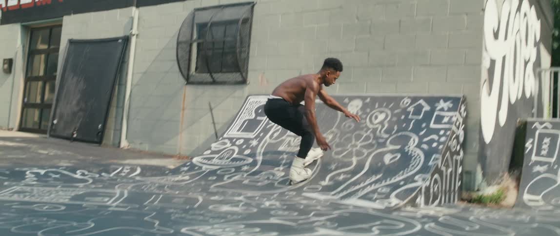 Shirtless black man rollerblading alone and doing a stunt on a ramp
