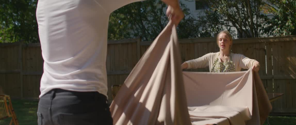 A man and a woman spreading a tablecloth on a table in a backyard