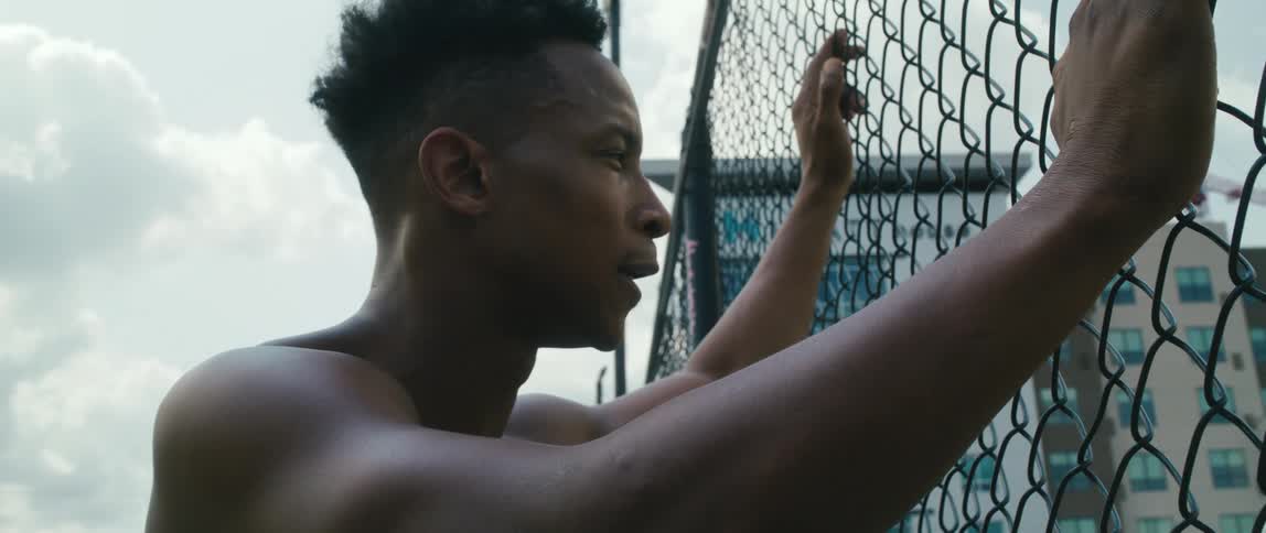 A young man holds onto a chain link fence while resting from exerting energy