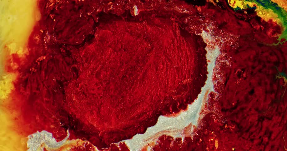 A red liquid under a microscope flowing outwards into other colors surrounding it