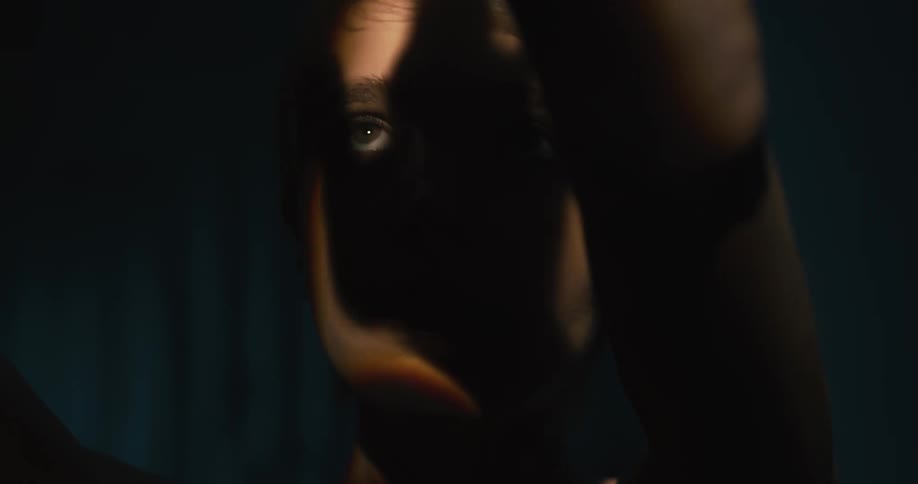 Young woman uses hands to cast shadows over her face in a dark room
