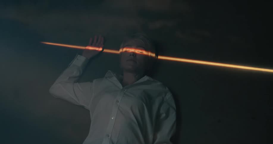 Light shining through narrow opening shines across eyes of person lying on her back in foggy shadowy room