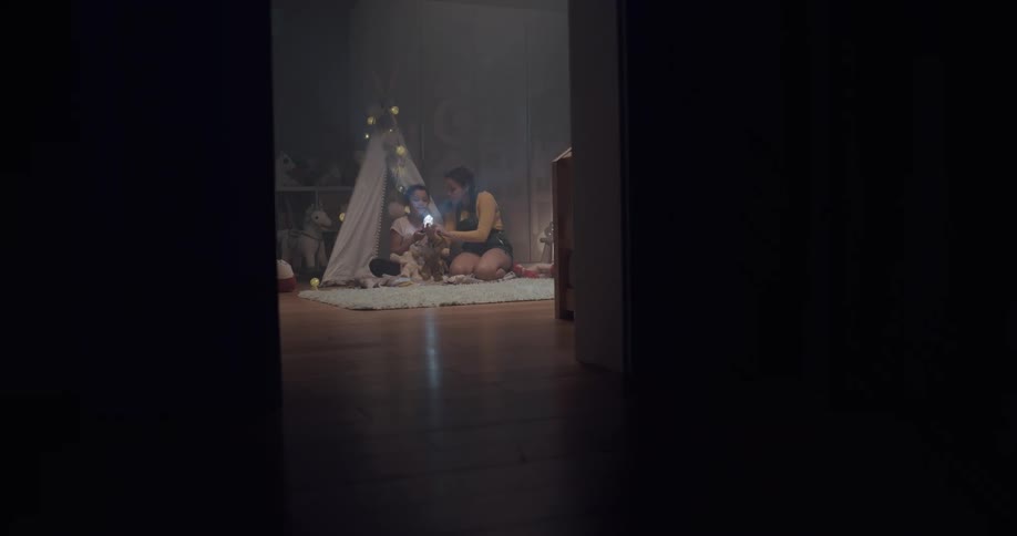 Sisters playing with flashlights inside a bedsheet tent in a bedroom at home