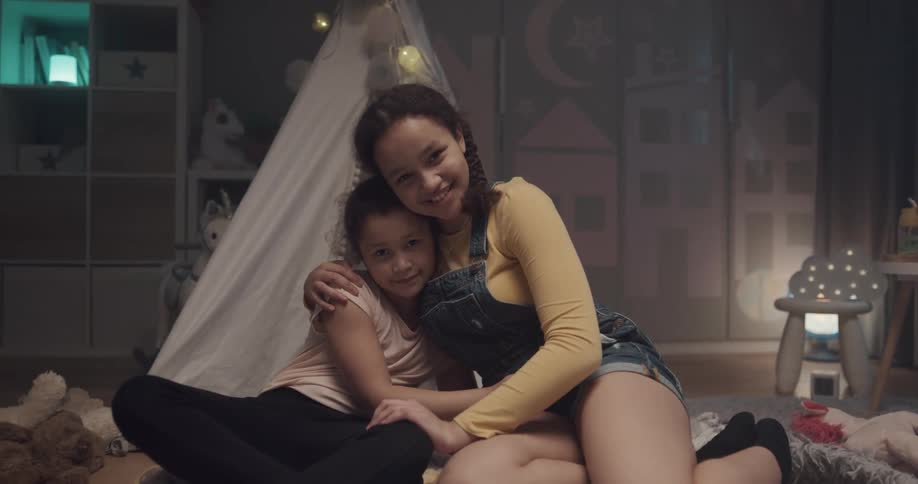 Two sisters are hugging while sitting in their room