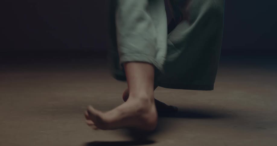 A barefoot woman wearing blue culottes dances in an empty room