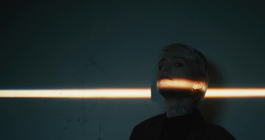 A woman standing and staring in a room next to a wall with light shining on her face