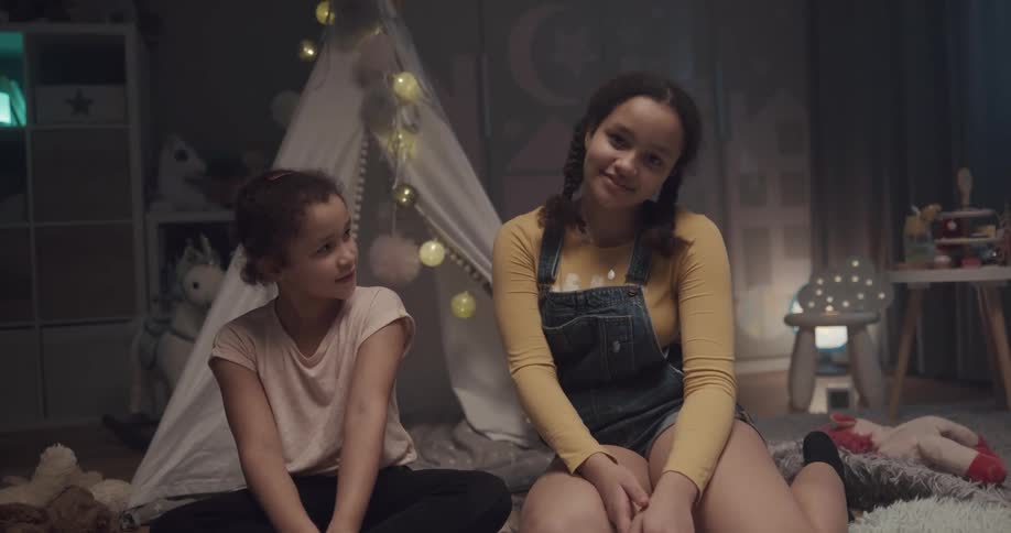 A child and teen sitting in a girls bedroom in front of tent smiling