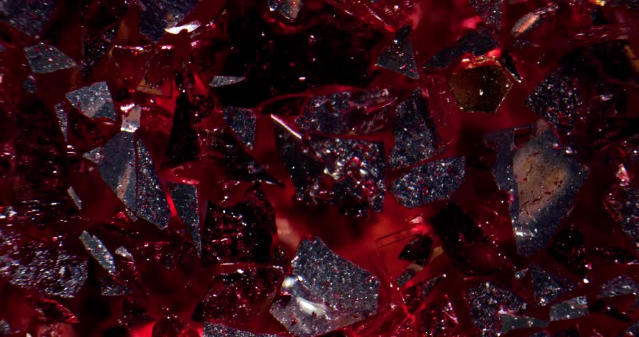 Pieces of red metallic sheets cut into abstract shapes hang over a black floor covered in glitter