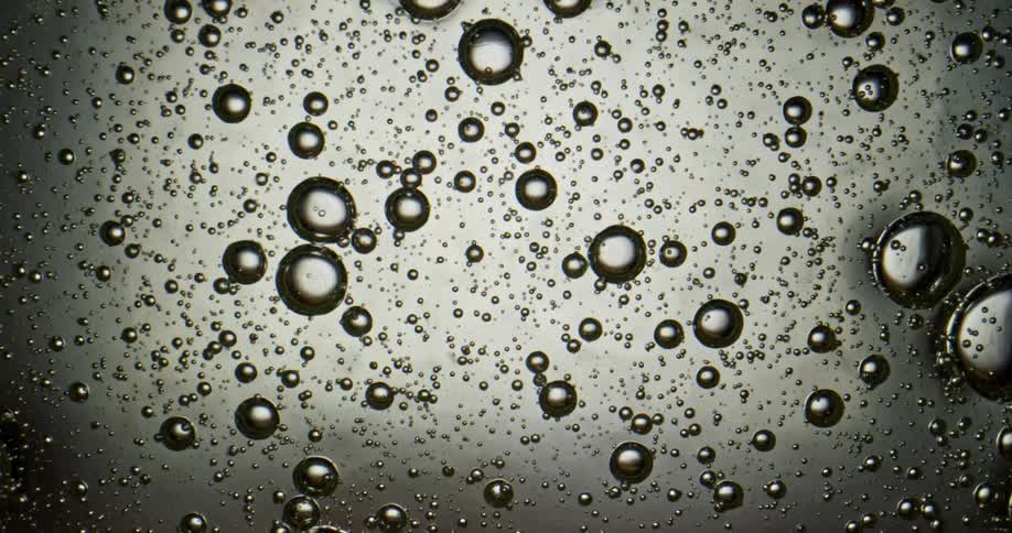 Bubbles in a clear light gray liquid move downwards under a microscope