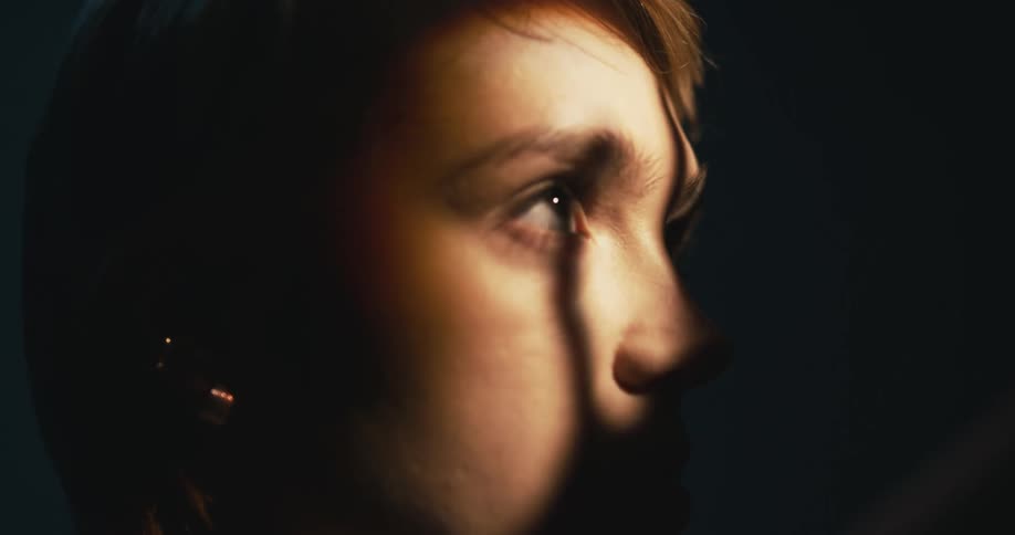 A teenage girl stands indoors as shadows move across her face