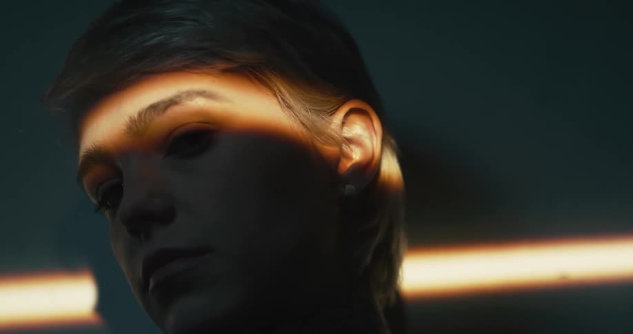 A horizontal beam of sunlight shines across a womans face as she stands indoors