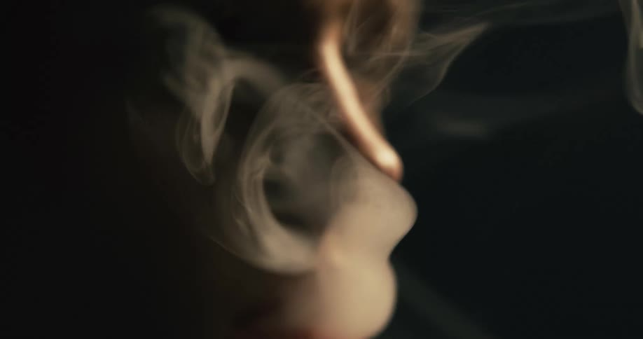 Person lights cigarette and smokes under light surrounded by darkness