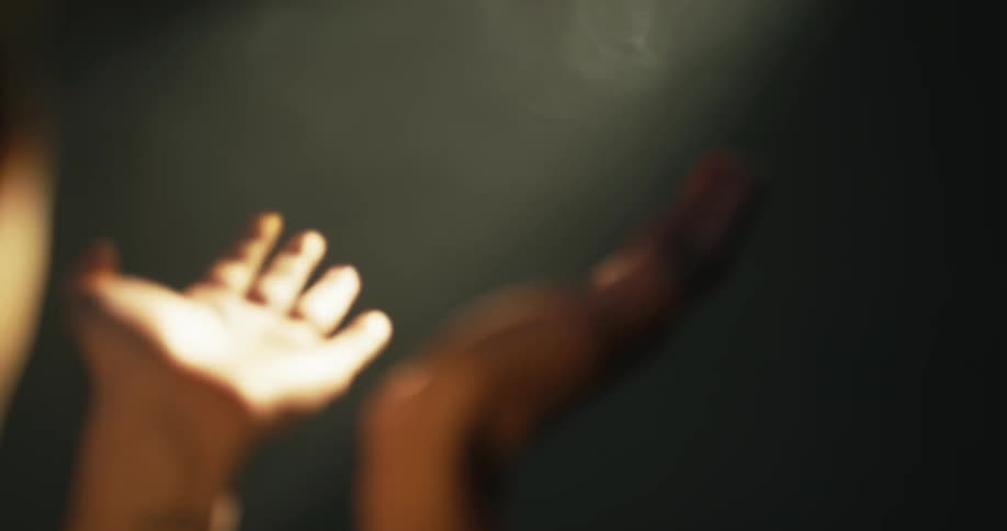 A woman staring up at a beam of light in a dark room moving her hands upwards in the light