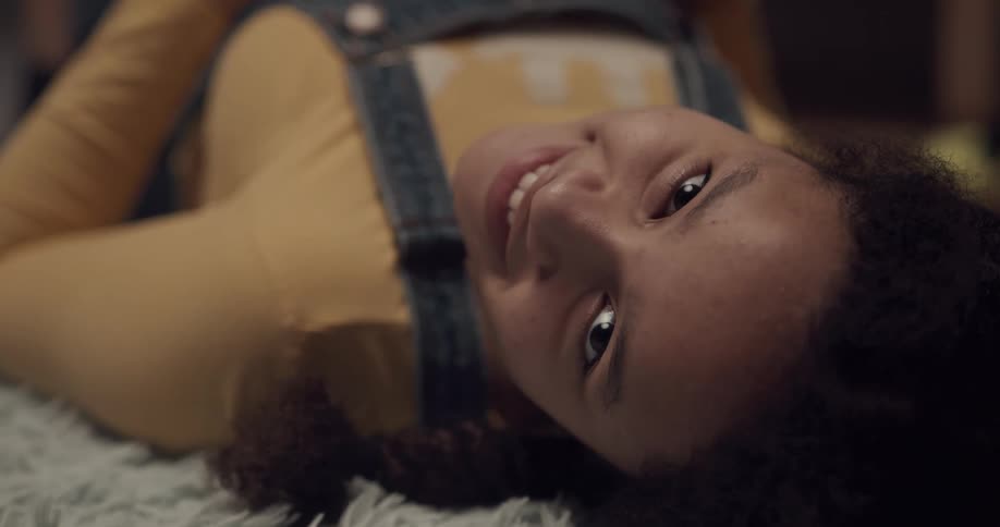 A young woman lying on a carpet shifts her eyes to look into the camera and smile