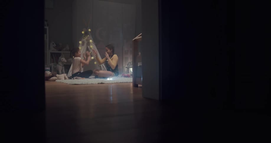 A pair of a girls play a clapping game together while sitting on a rug in a room in a house