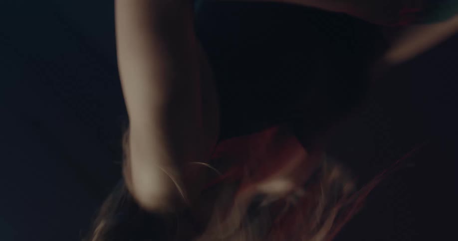 A long haired female dancing in a darkness with a few bright lights shining