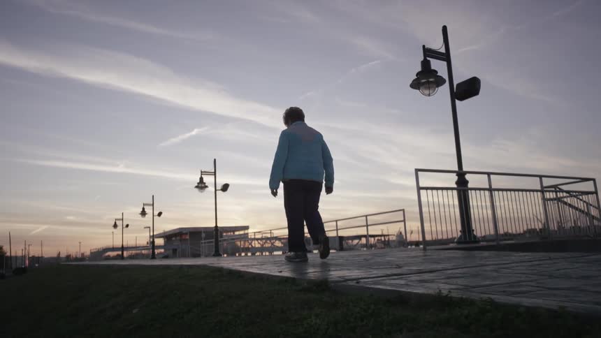 Woman walking on a city pathway next to water at sunset