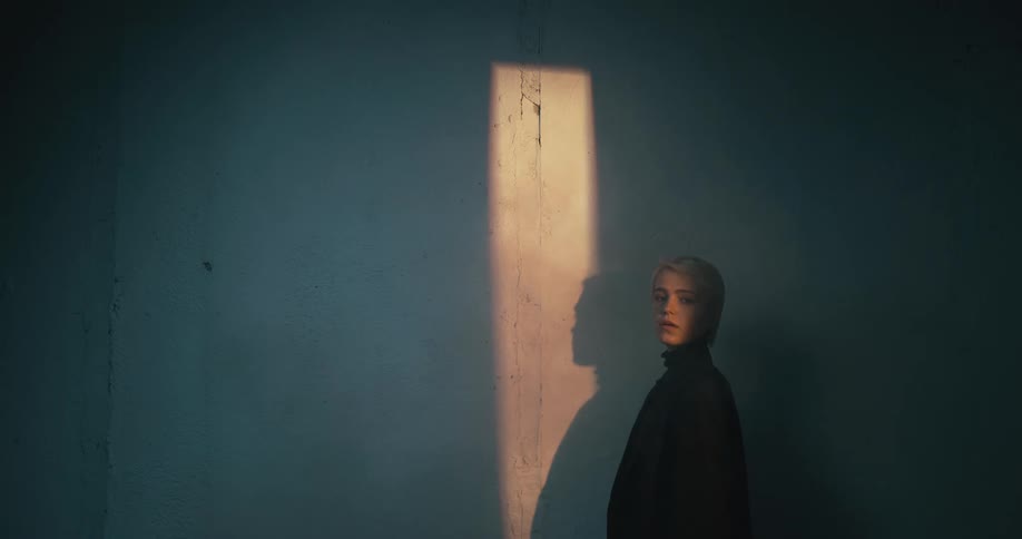 Woman stands next to wall near light cast onto wall throughrectangular opening