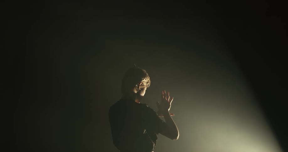 A woman standing in a dark room in front of a beam of light moving her hands around in front of it
