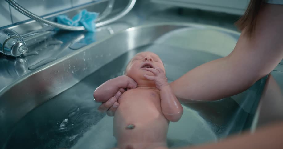 A woman is cleaning a newborn in the hospital bath