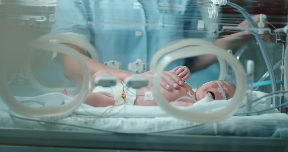 A newborn receiving respiratory help and comforted by another person while in the hospital