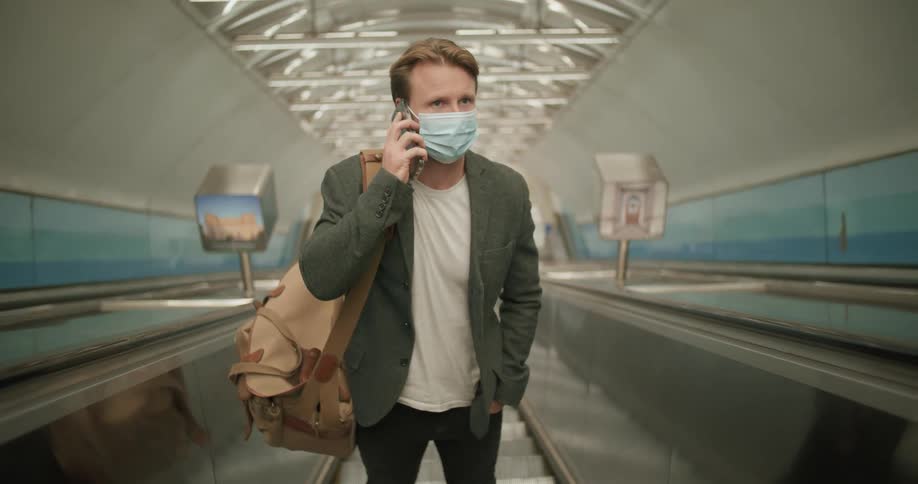 Man wearing a face mask answer a call on his smartphone while riding an scalator